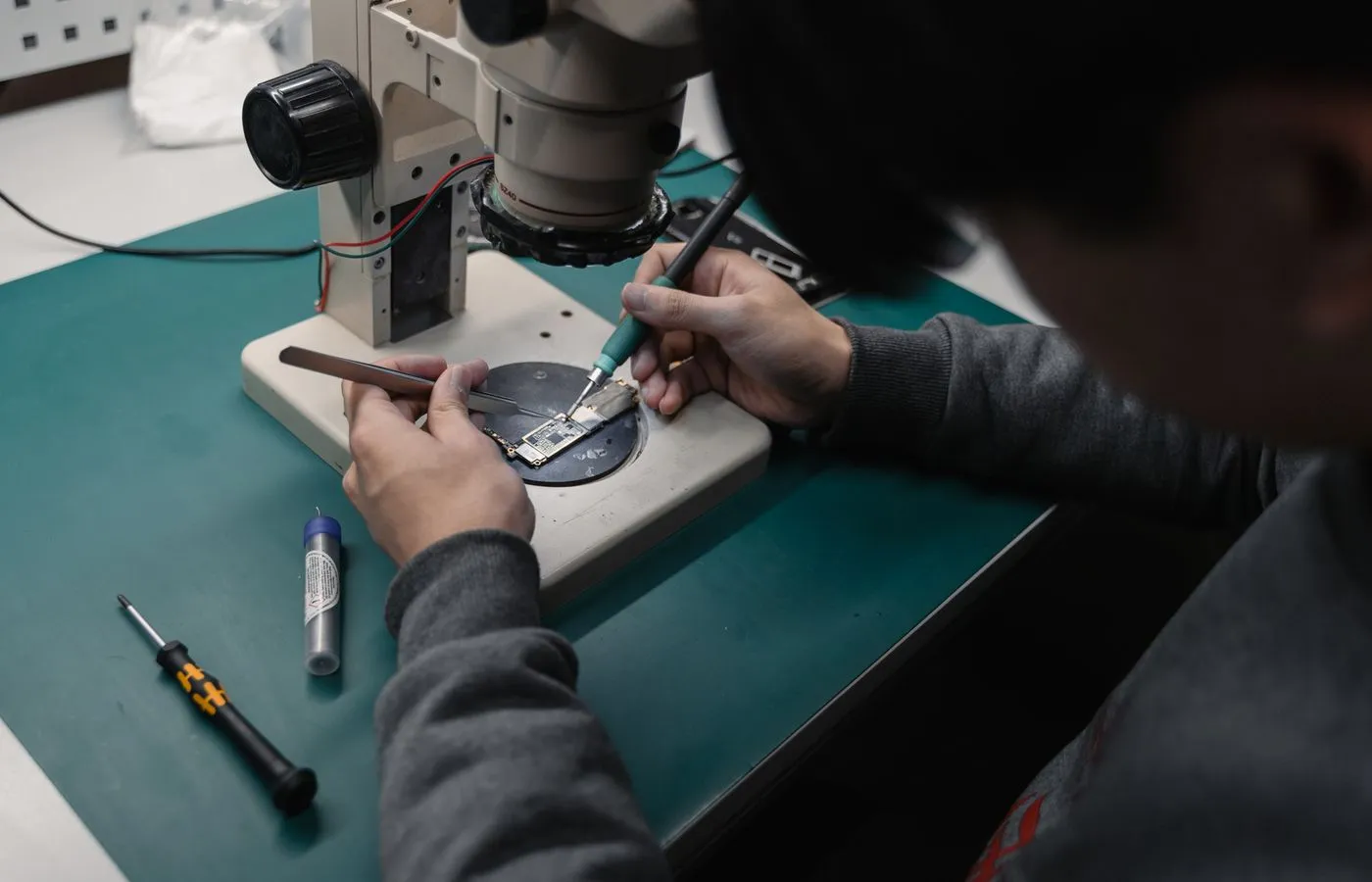 Technician examining a populated circuit board through a laboratory microscope