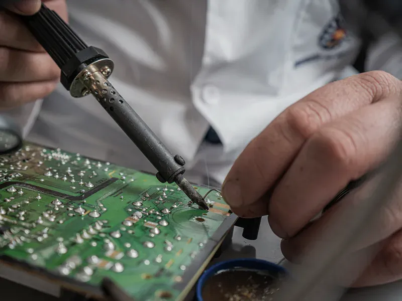 Technician soldering a circuit board during pin-compatible component replacement qualification